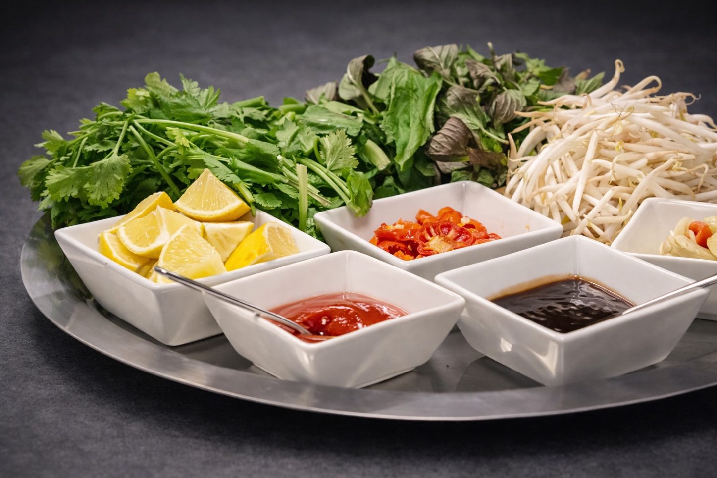 Platte mit frischen Kräutern, Sojasprossen, Zitrone, Chili und Dip-Schälchen