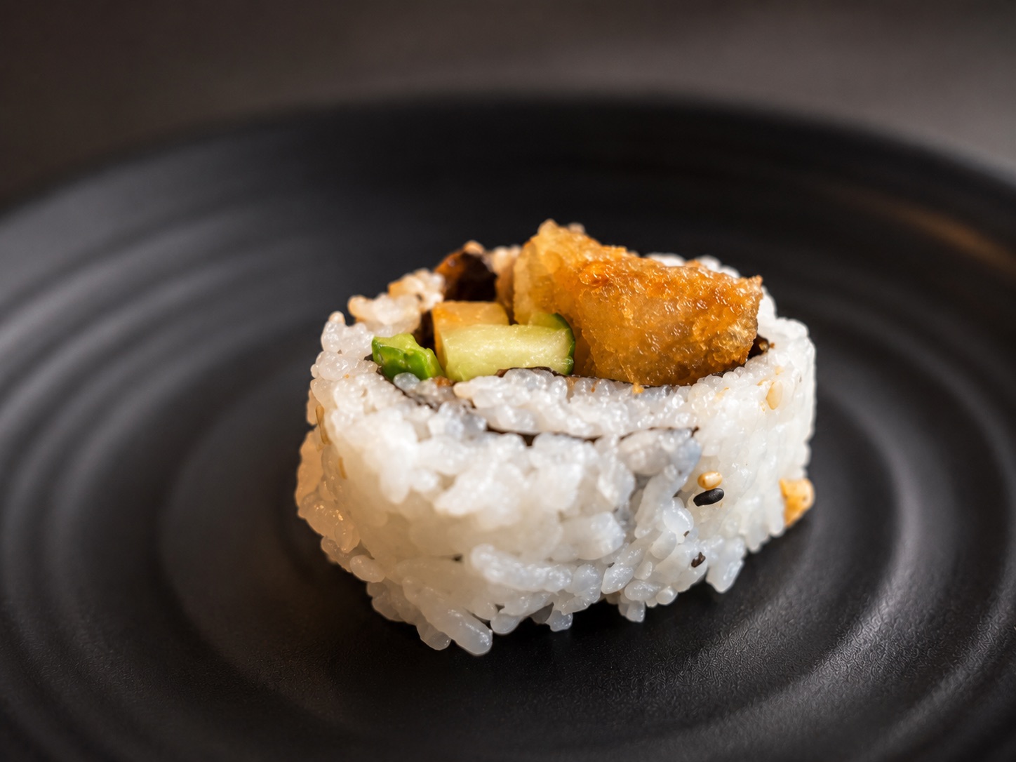 Inside-Out-Rolle mit Tempura-Füllung auf schwarzem Teller